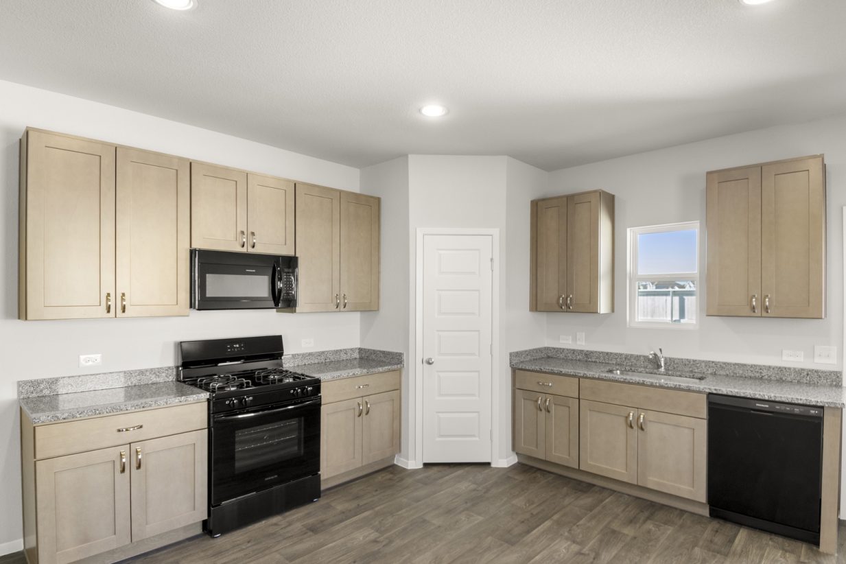 Image of a L-shaped kitchen with light brown cabinets, granite countertops, and black appliances