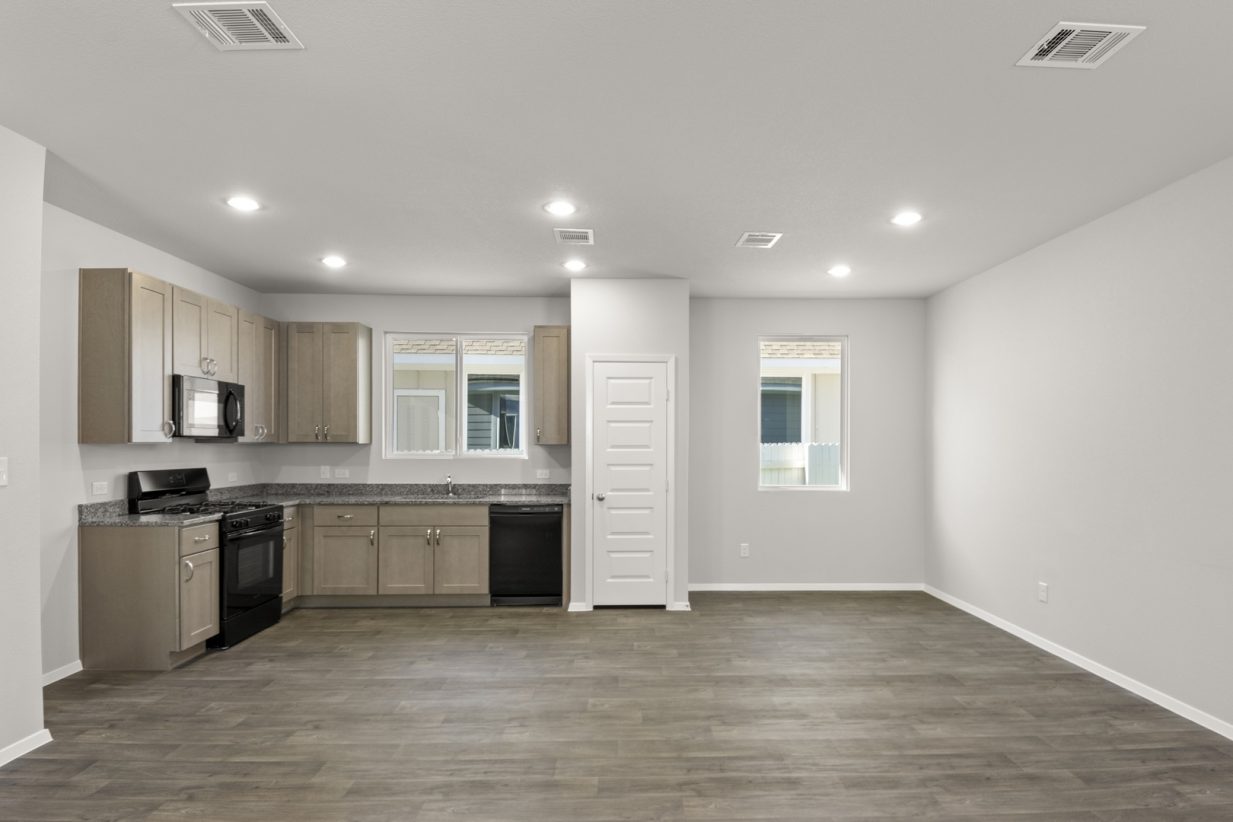 Image of a kitchen/dining area with dark vinyl flooring, a L-shaped kitchen with granite countertops and light brown cabinets