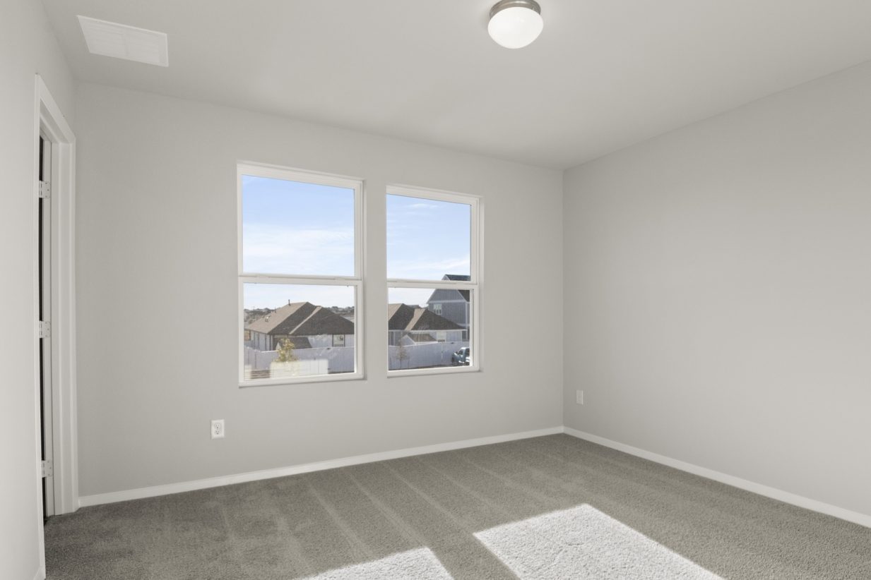 Image of a primary bedroom with tan carpeting, light grey walls and two windows