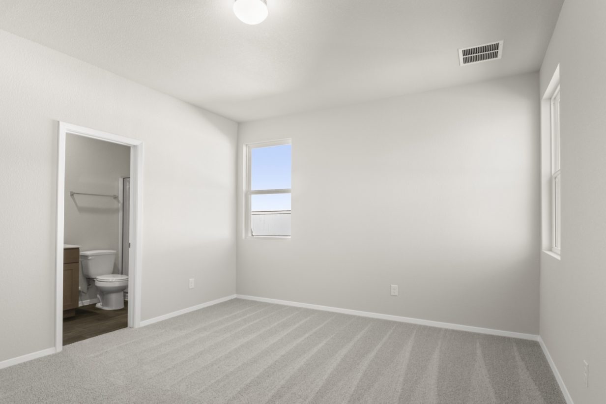 Image of a primary bedroom with tan carpeting and cream colored walls and a door connecting to the primary bathroom