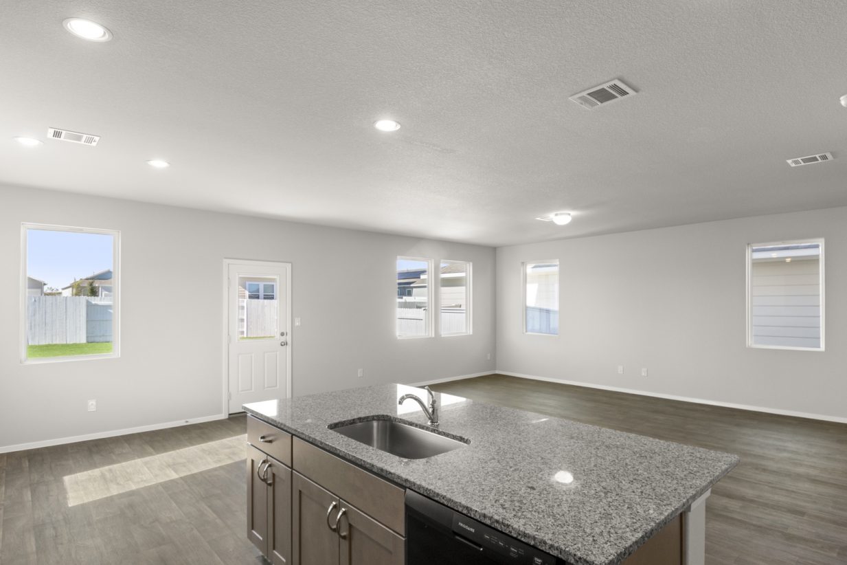 Image of a kitchen and living overview with a granite center island and light brown cabinets