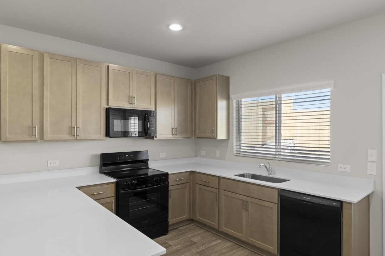 Image of a U-shaped kitchen with a white countertop, brown cabinets, black appliances, and a window above the sink