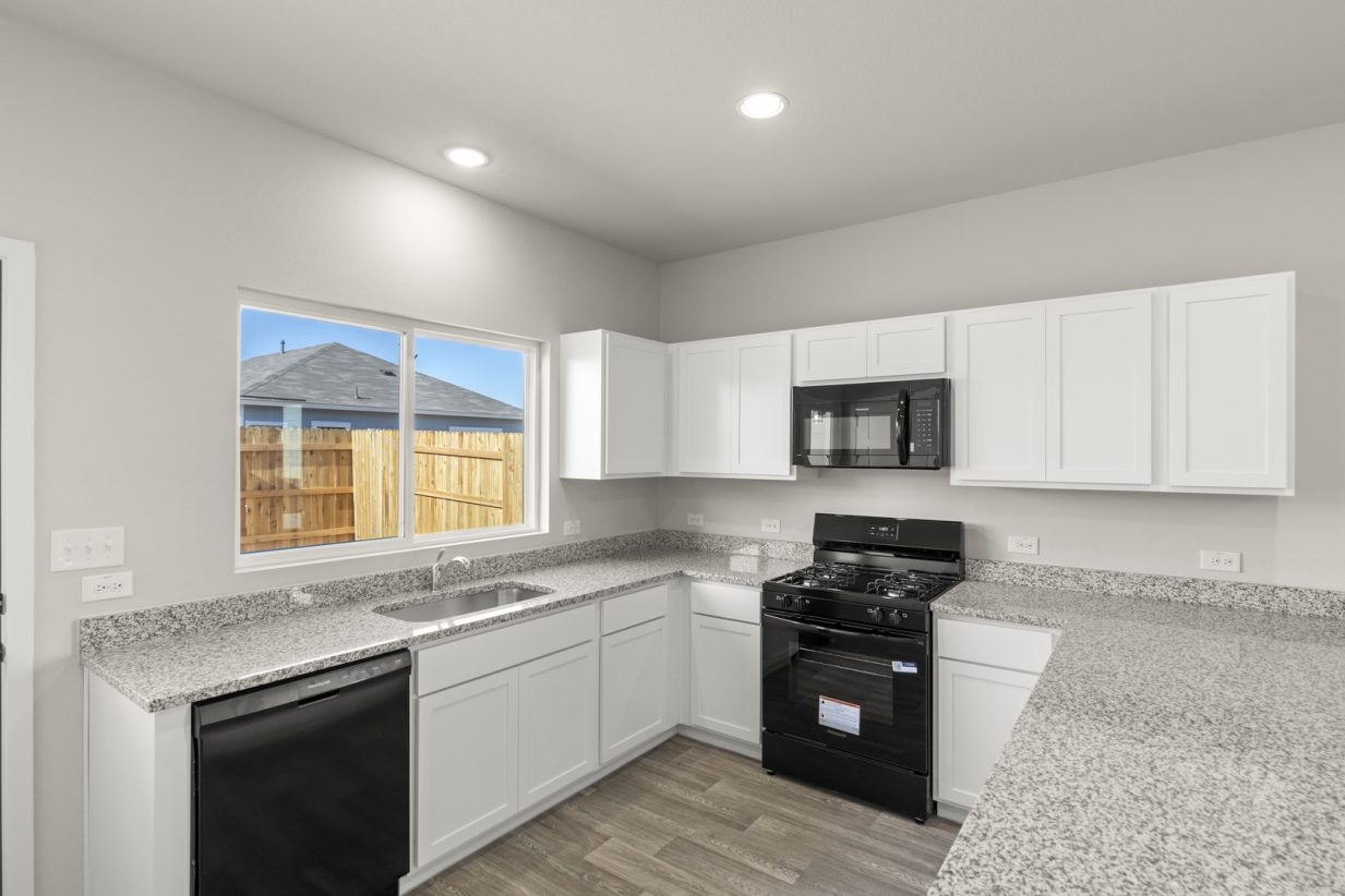 Image of a U-shaped kitchen with white cabinets, black appliances, a window above the sink, and white trim