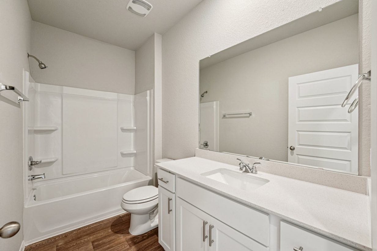 Image of a bathroom with a dual vanity, white cabinets, a mirror and a shower with a tub