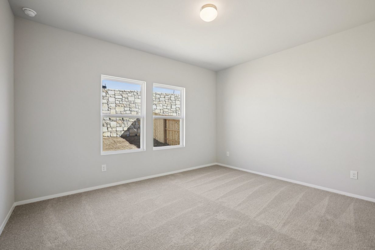 Image of a primary bedroom with light grey walls, tan carpeting, windows and white trim