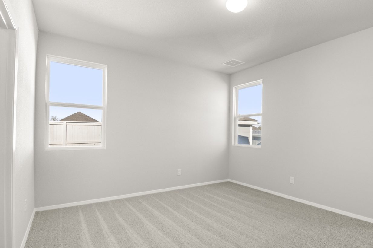 Image of a primary bedroom with tan carpeting and light grey walls with two windows in the corner of the room
