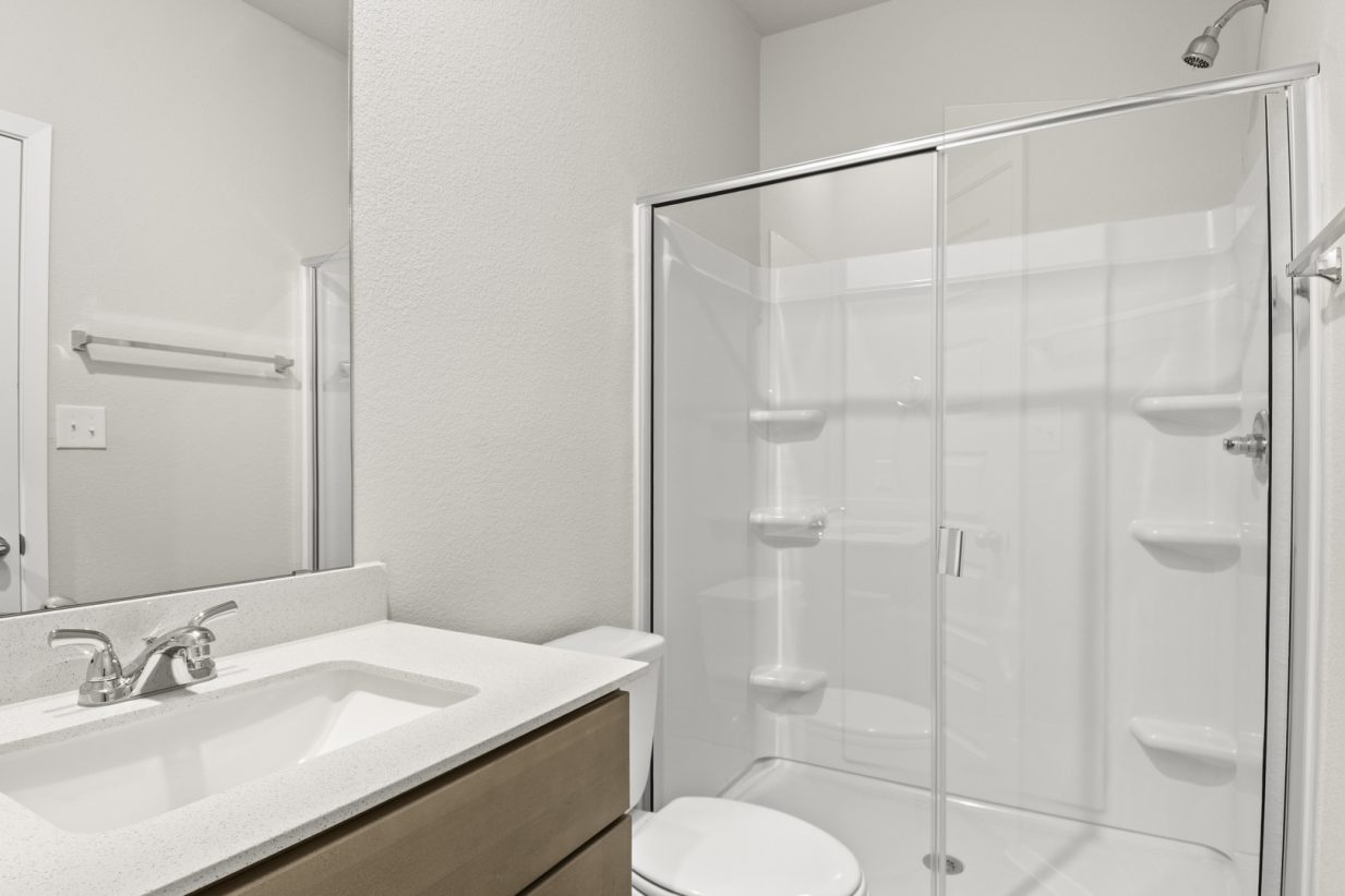 Image of a primary bathroom with brown cabinets, a white vanity and a walk-in shower