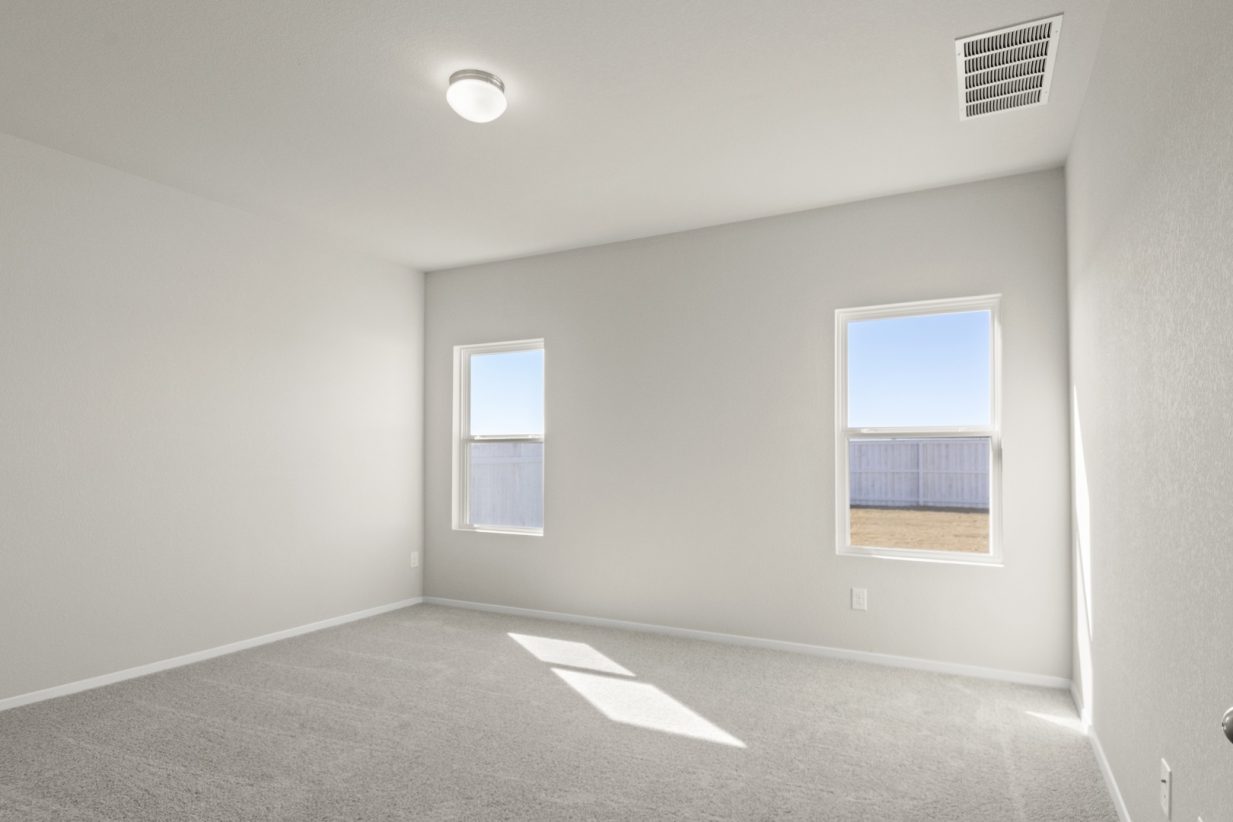Image of a primary bedroom with cream walls, tan carpeting, two windows, and white trim