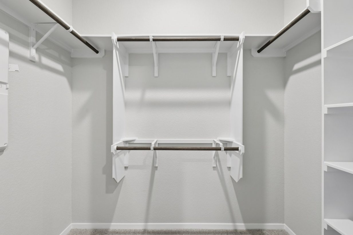 Image of a primary closet with white shelves and trim
