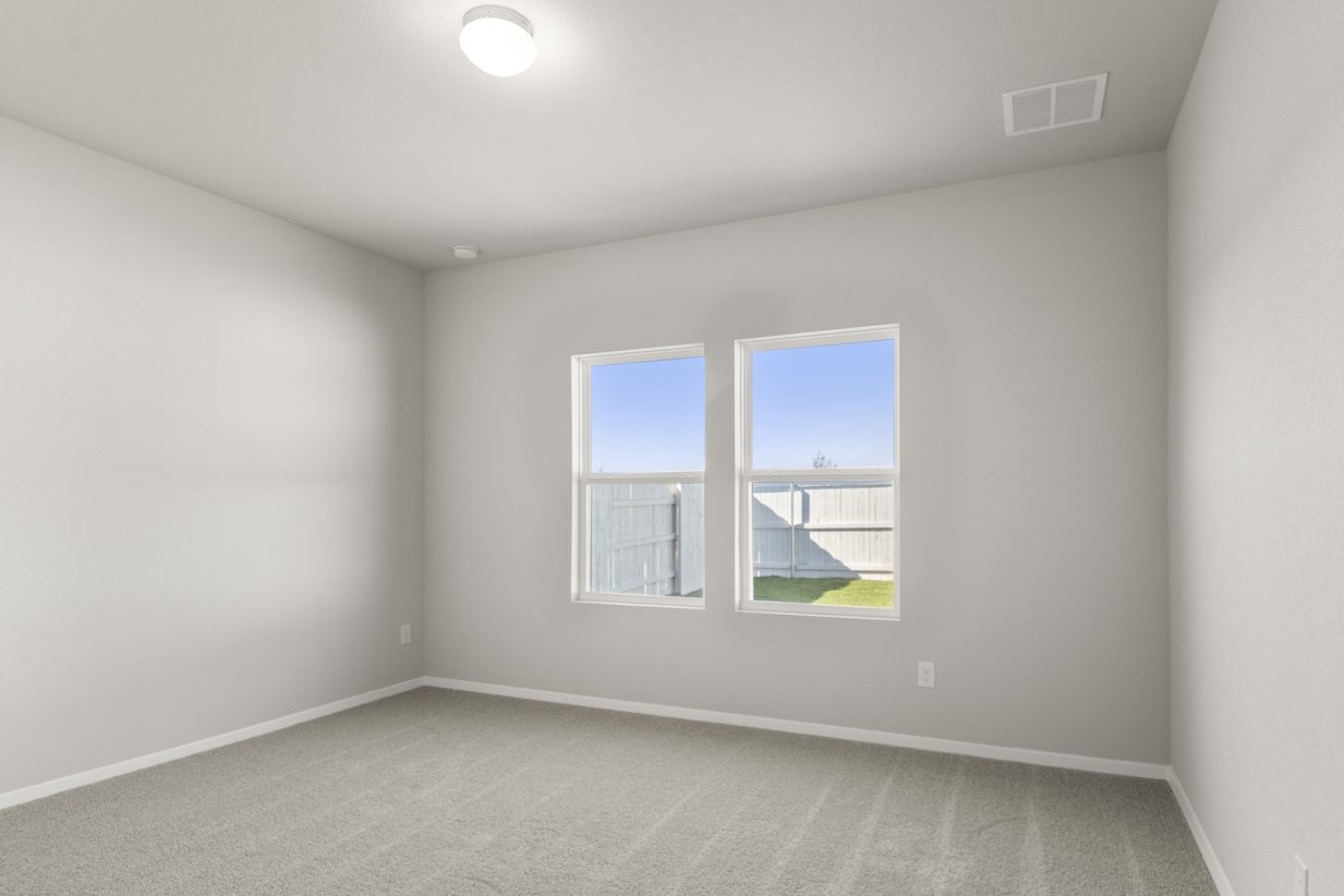 Image of a primary bedroom with tan carpeting, light grey walls and two windows