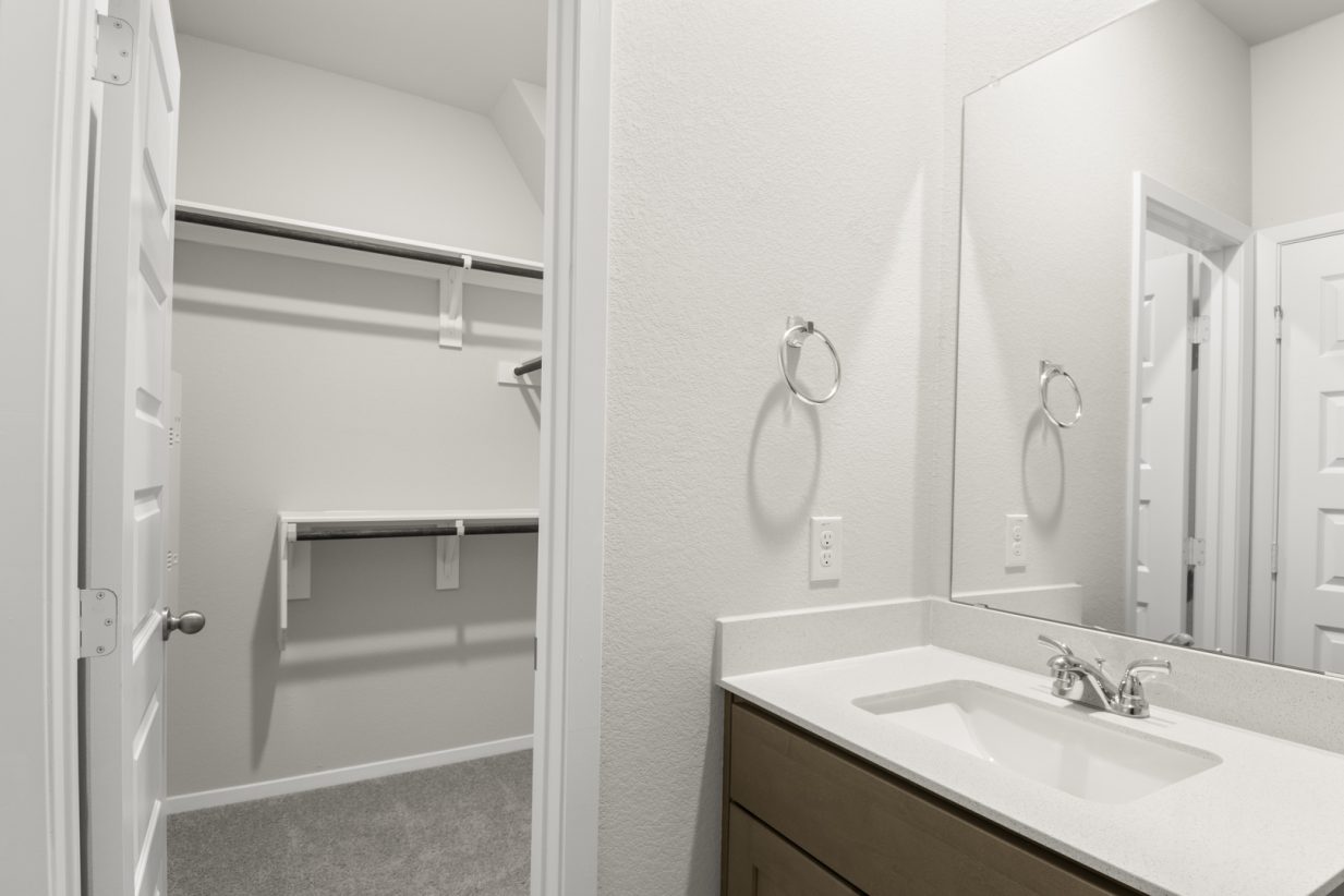 Image of a primary bathroom with a connecting walk in closet and a white vanity