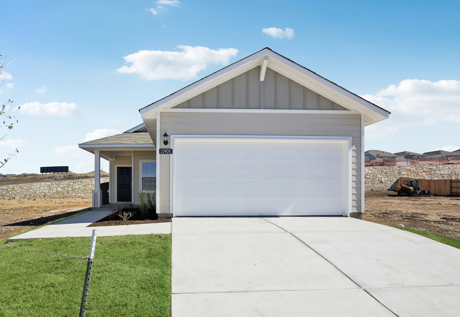 Image of a grey one story house with a white garage, a cement driveway, green grass and a blue sky in the background