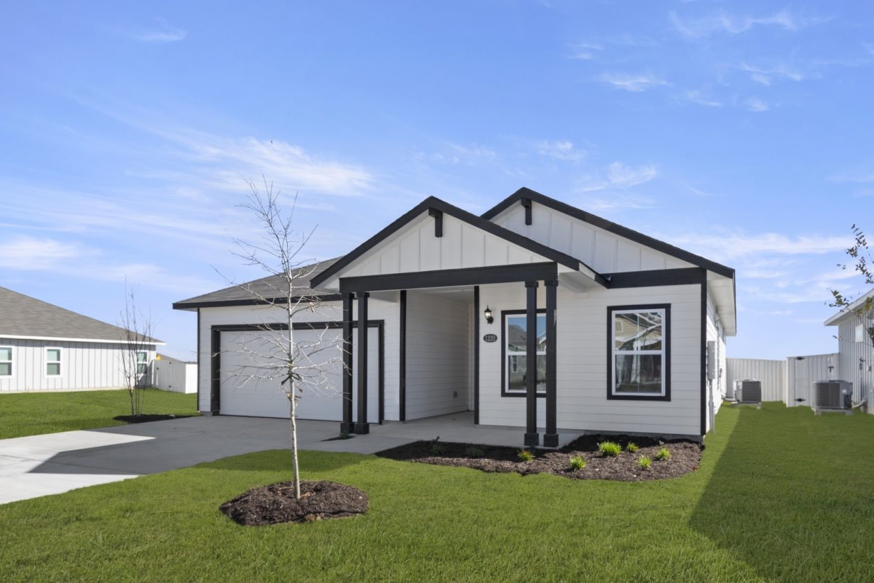 Image of a white one story house with black trim, a white garage, a cement driveway, green grass front yard and a blue sky in the backgrounf