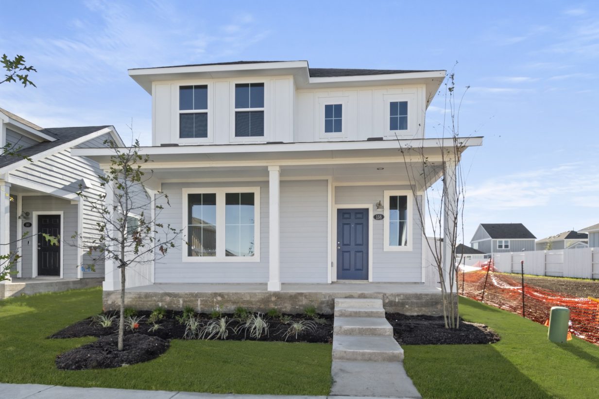 Image of the front exterior of a two story light grey and white home with white trim, a dark blue front door, a front porch and a cement pathway