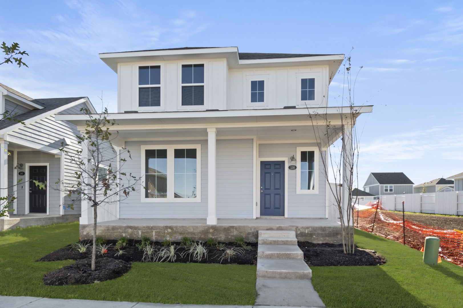 Image of the front exterior of a two story light grey and white home with white trim, a dark blue front door, a front porch and a cement pathway