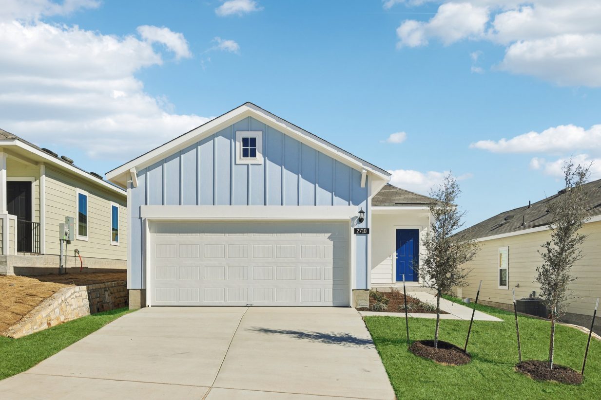 Image of a blue one story home with a white garage door, royal blue front door, a cement driveway, a green grass front yard, and a blue sky in the background