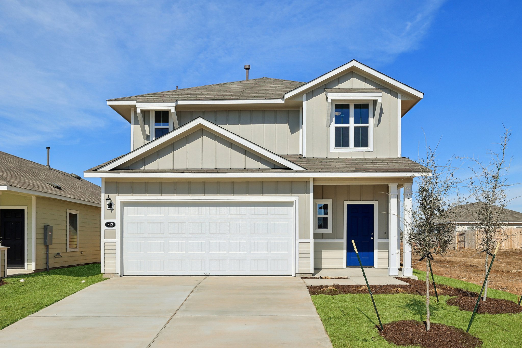 Image of a front exterior two story beige house with a royal blue front door, a white garage door, a cement driveway and a blue sky in the background