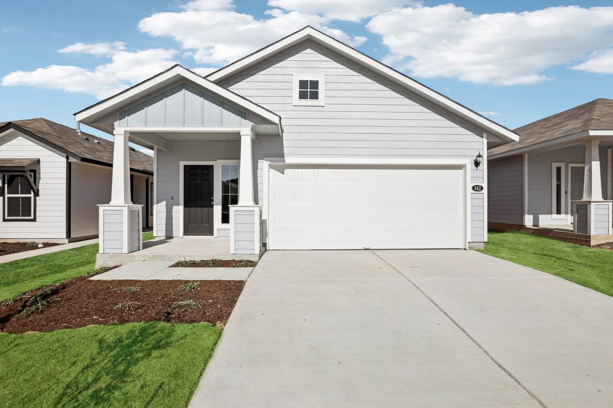 Image of the front exterior of a grey one story home with a white garage, brown door, a cement driveway, and a blue sky in the background