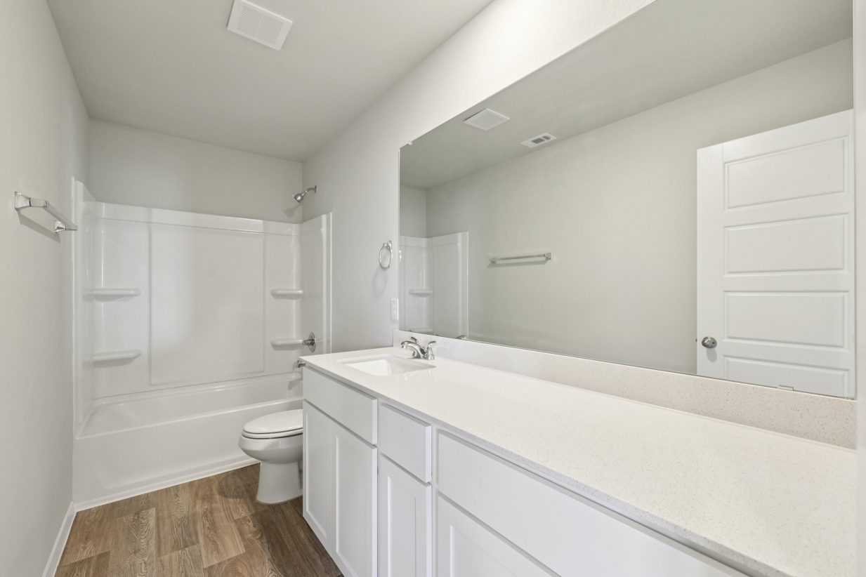 Image of a bedroom with a dual vanity, white cabinets, a large mirror and a shower and tub
