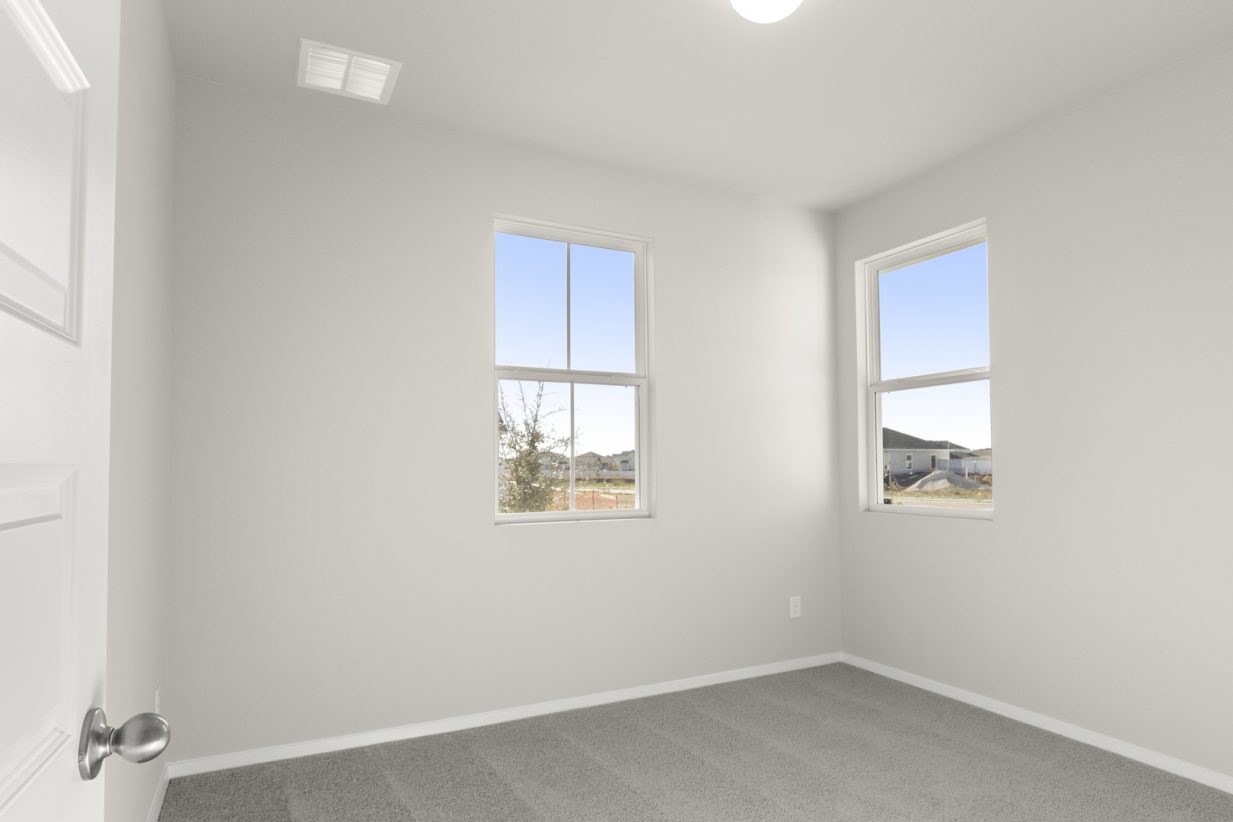 Image of a bedroom with tan carpeting and light grey walls with two windows