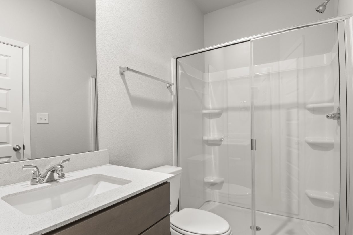 Image of a primary bathroom with a white vanity and large mirror, and a white vinyl walk-in shower