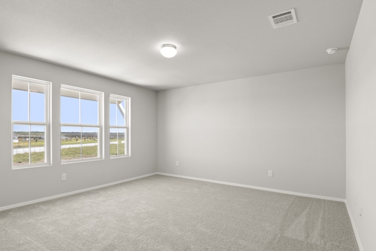 Image of a bedroom with tan carpeting, light grey walls, and three windows