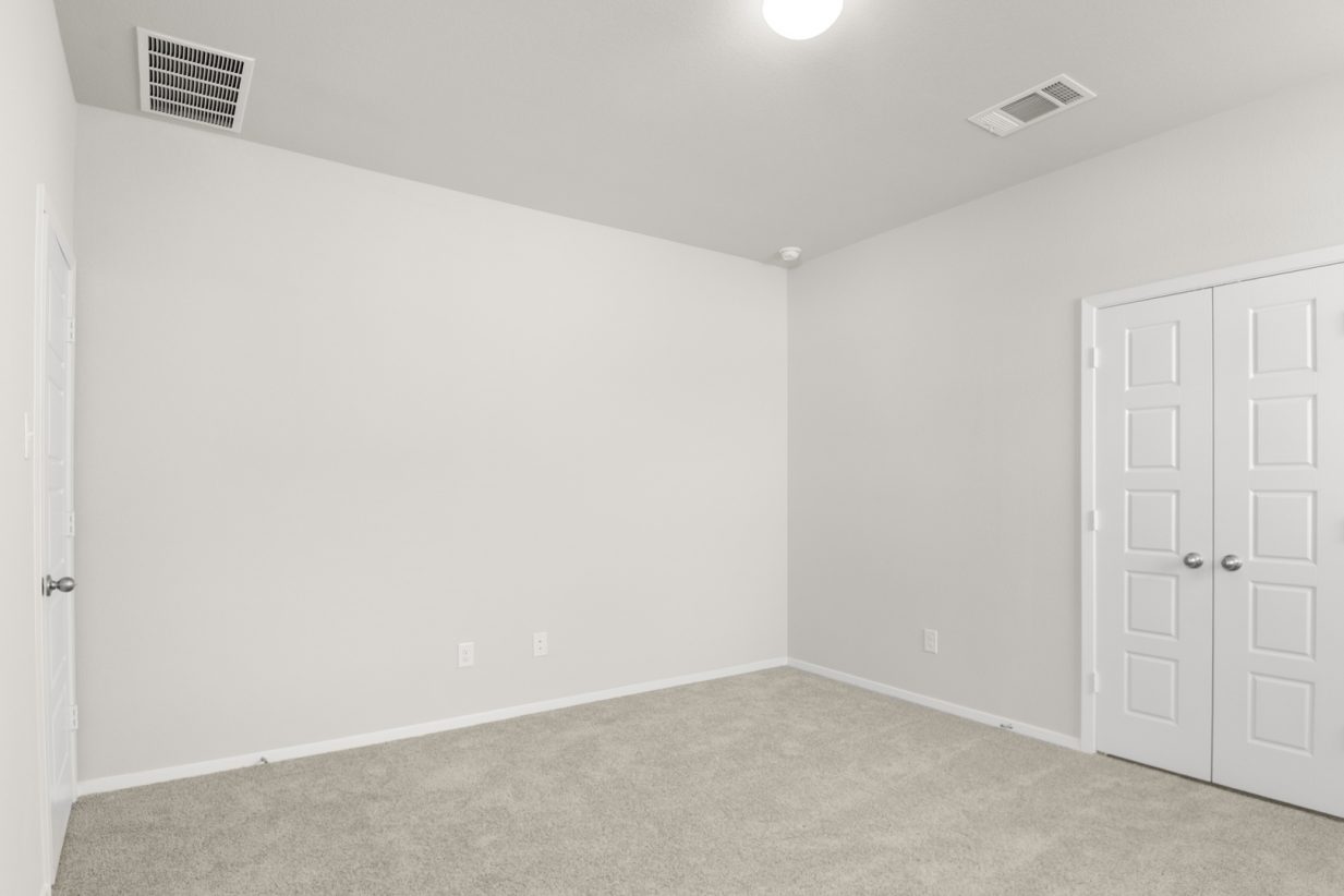 Image if a primary bedroom with tan carpeting, light grey walls, and double doors that lead to a primary bathroom