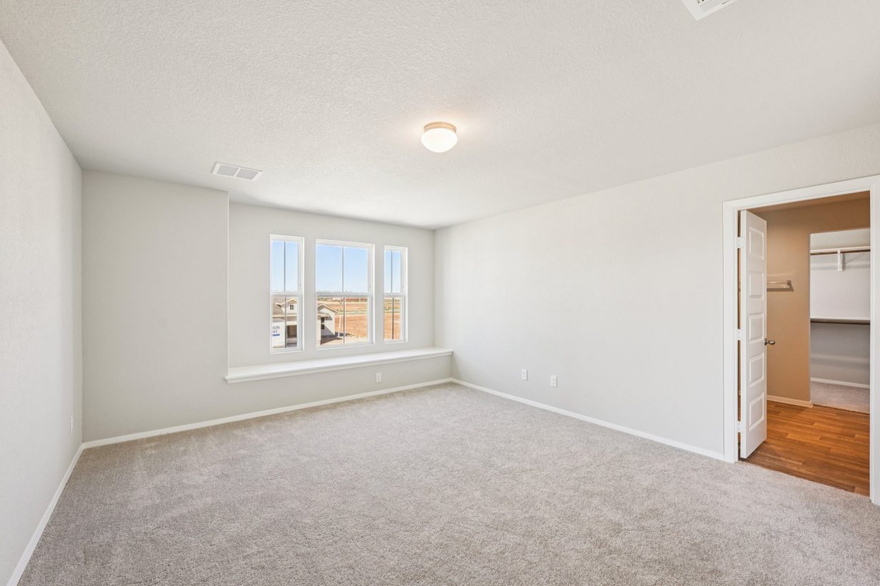 Image of a primary bedroom with beige walls, tan carpeting, and windows with a window seal