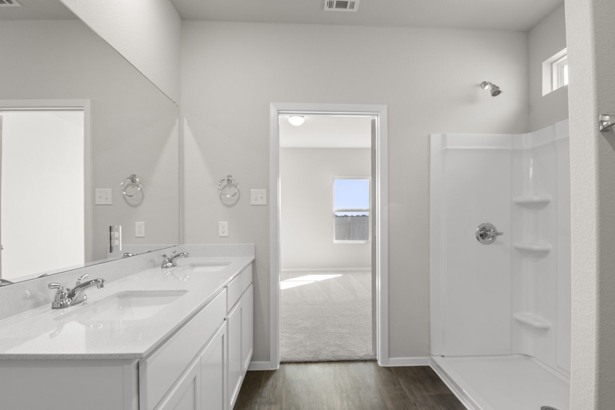 Image of a primary bathroom with light grey walls, white trim, white cabinets, jack and jill vanity, large mirror and a white walk-in shower