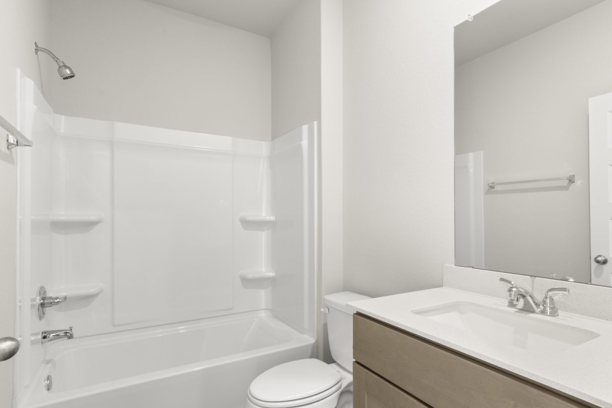 Image of a bathroom with a white vinyl shower and tub with a white vanity with a mirror and brown cabinets