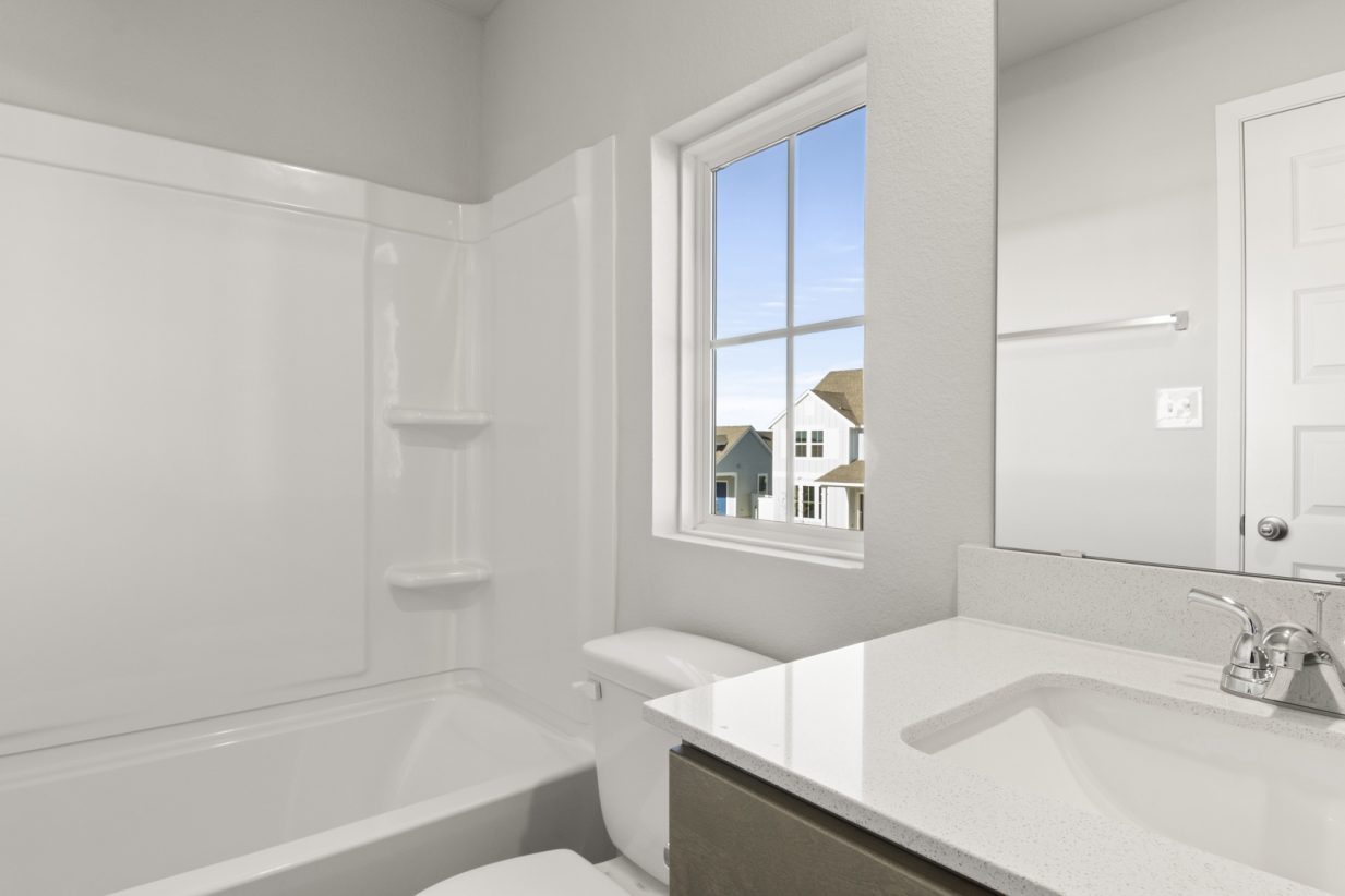 Image of a bathroom with a white vinyl shower and tub, a white vanity and a window
