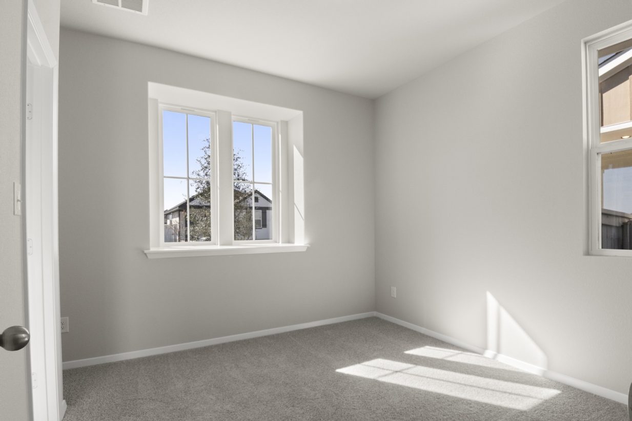 Image of a bedroom with light grey walls, tan carpeting, two windows and white trim