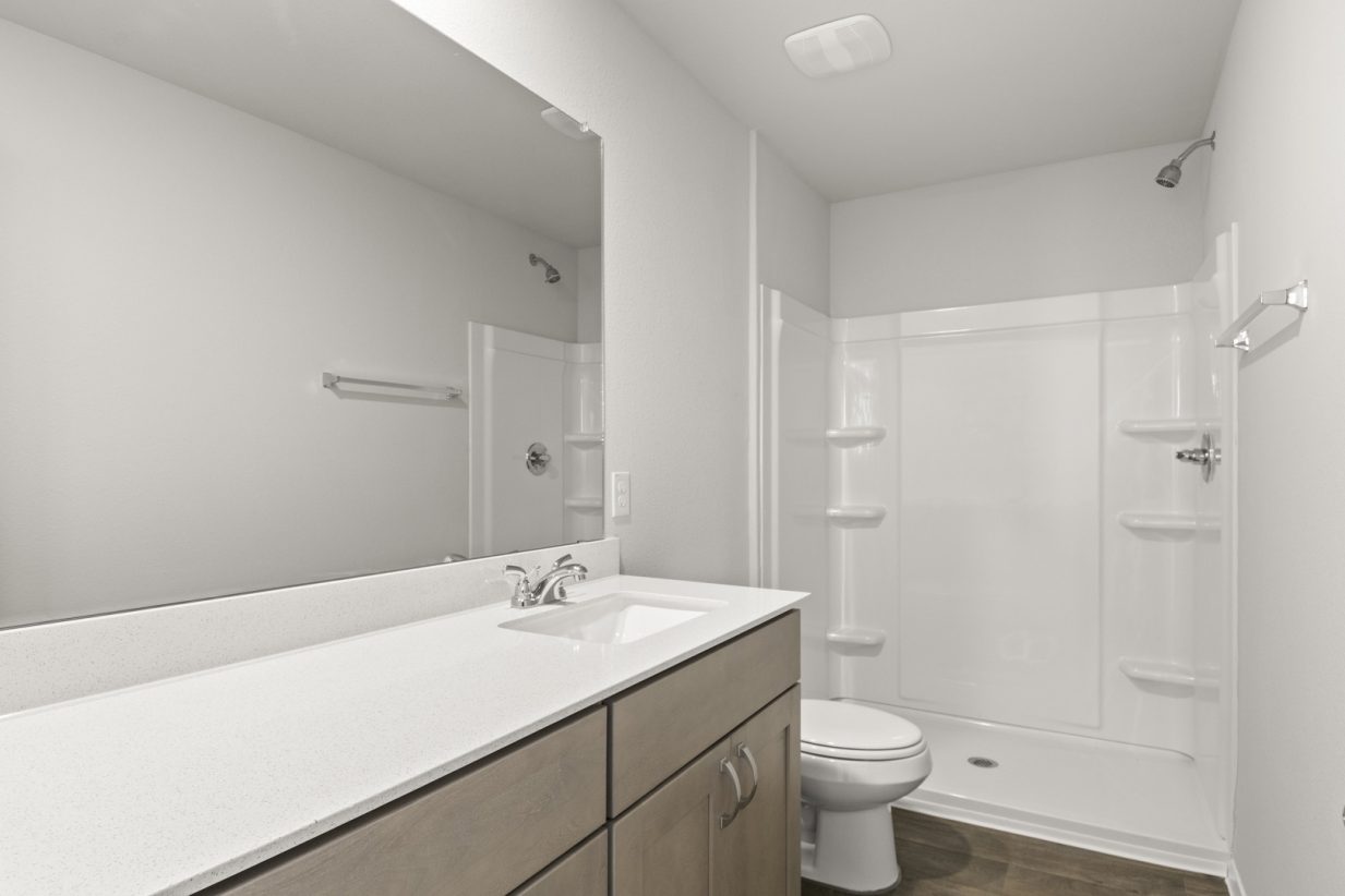 Image of a primary bathroom with a white double vanity, light brown cabinets and a white walk-in shower