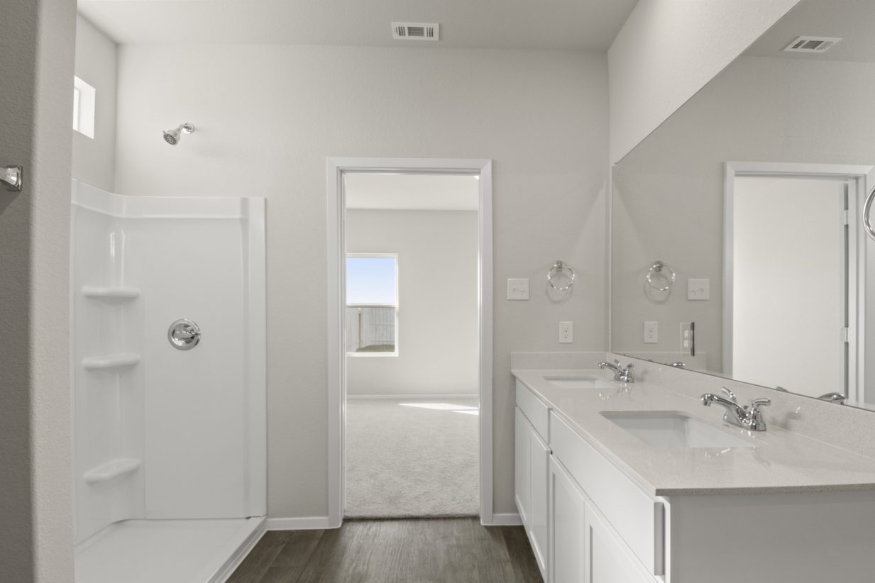 Image of a primary bathroom with cream walls, white cabinets, a white jack and jill vanity, a large mirror and a walk-in shower