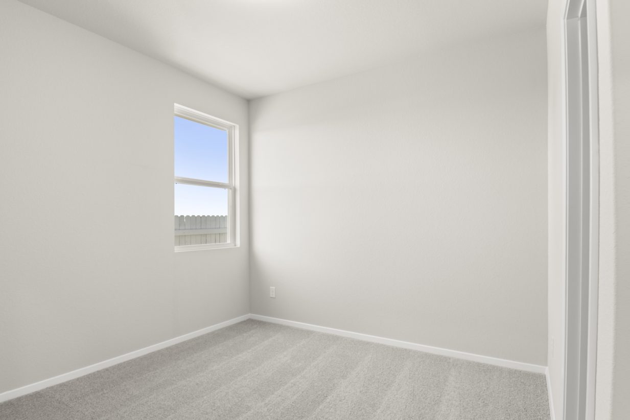 Image of a bedroom with tan carpeting, light grey walls and a window