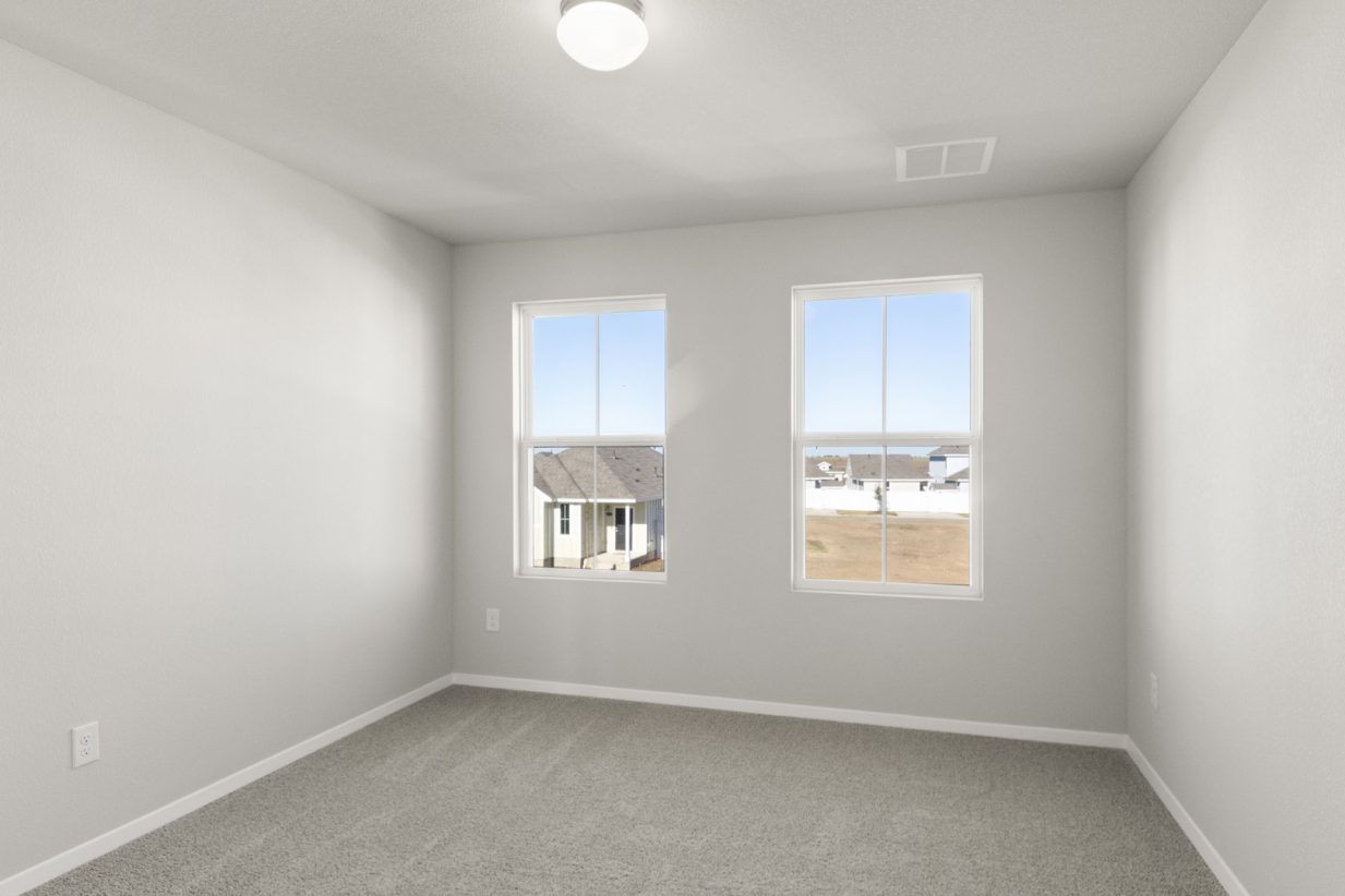 Image of a bedroom with tan carpeting, light grey walls and two windows