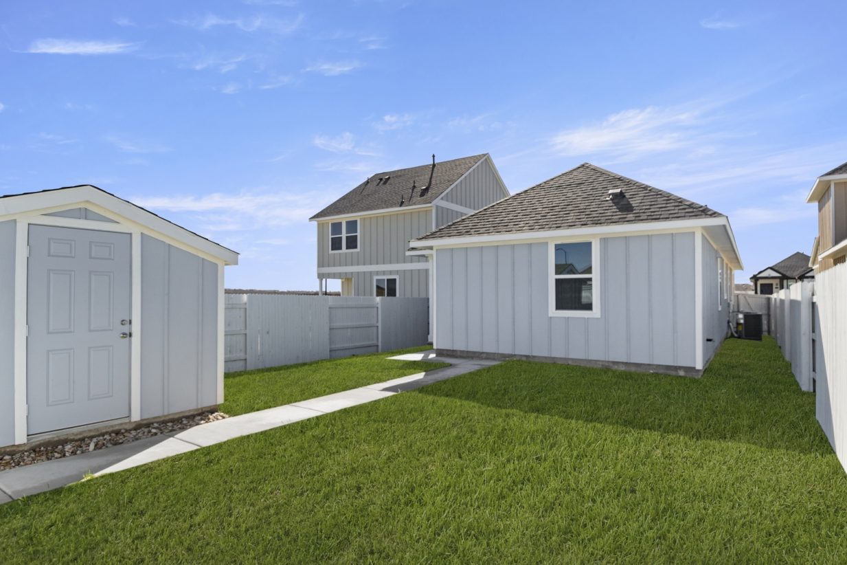 Image of the back exterior of a blue one story home with a green grass backyard, a blue shed, and a white fence