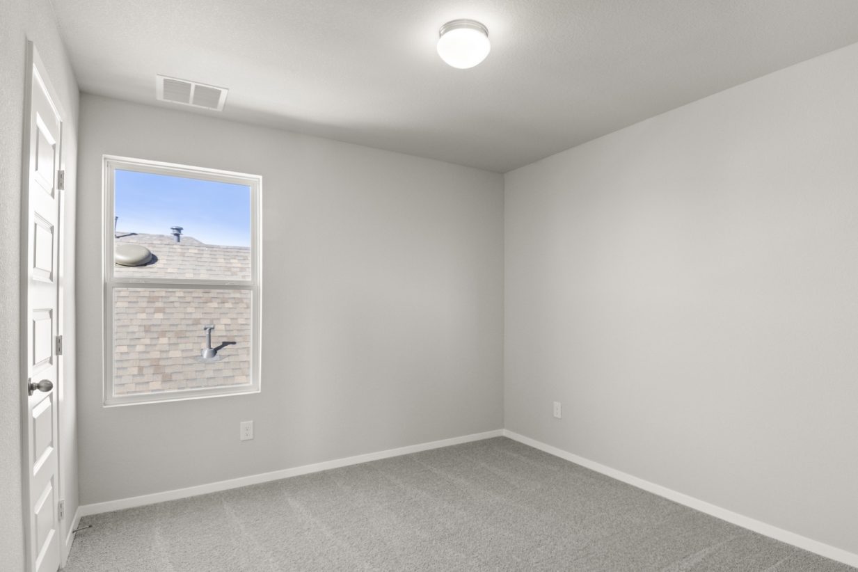 Image of a bedroom with light grey walls, tan carpeting, and a window