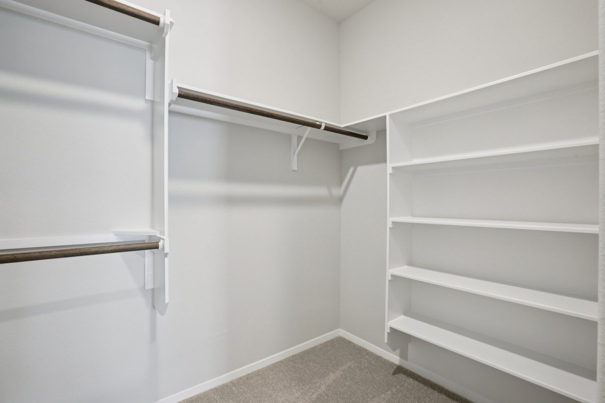 Image of a primary closet with white shelves, and wooden rods
