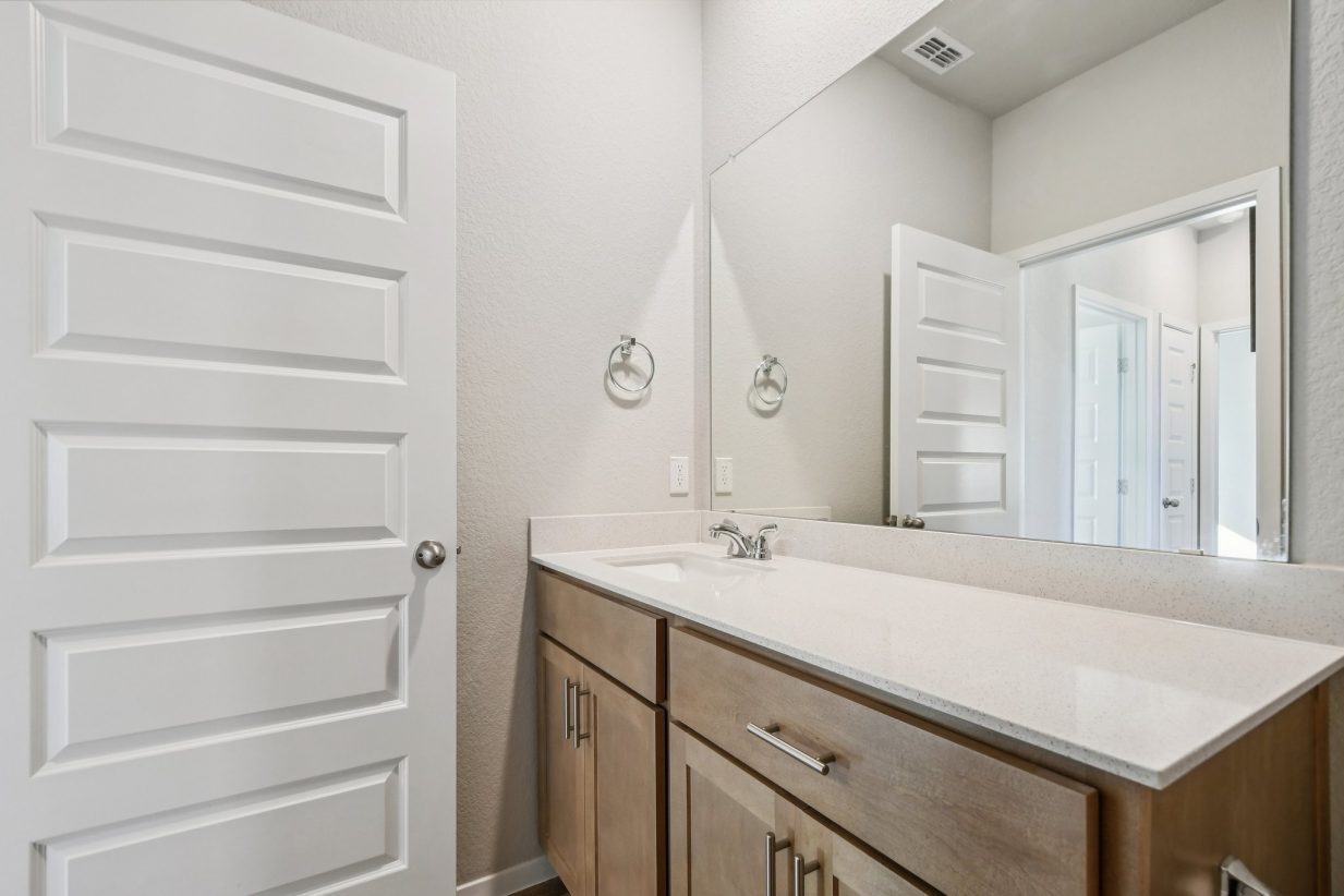 Image of a bedroom with brown cabinets, a large mirror and a white dual vanity