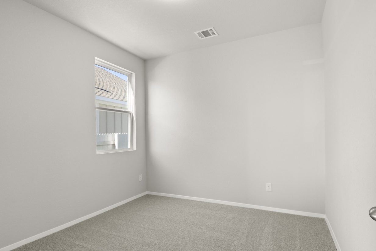 Image of a bedroom with tan carpeting and light grey walls with a window