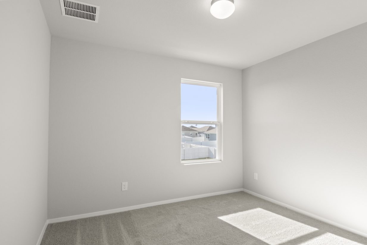 Image of a bedroom with tan carpeting with light grey walls and a window