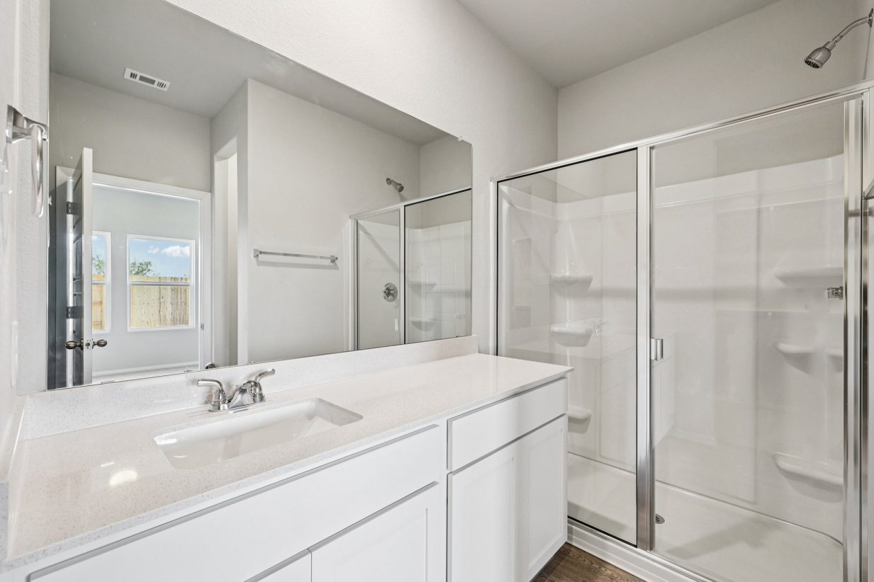 Image of a primary bedroom with a white vanity, a large mirror, white cabinets and a walk-in shower