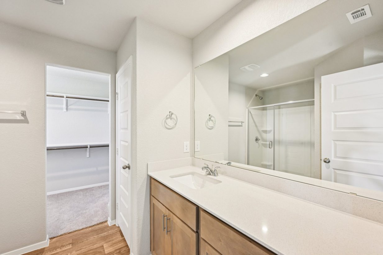 Image of a primary bathroom with a dual vanity, a large mirror and a closet