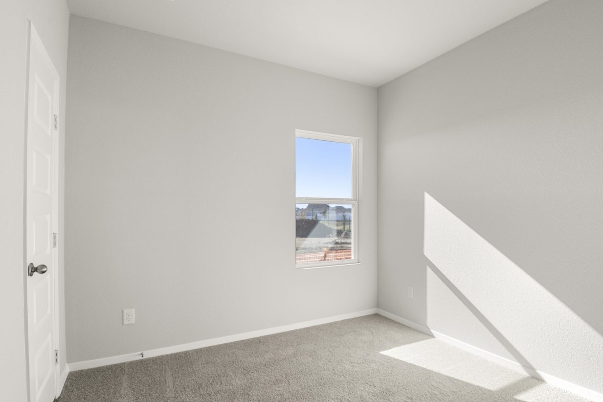 Image of a bedroom with light grey walls, tan carpeting and a window