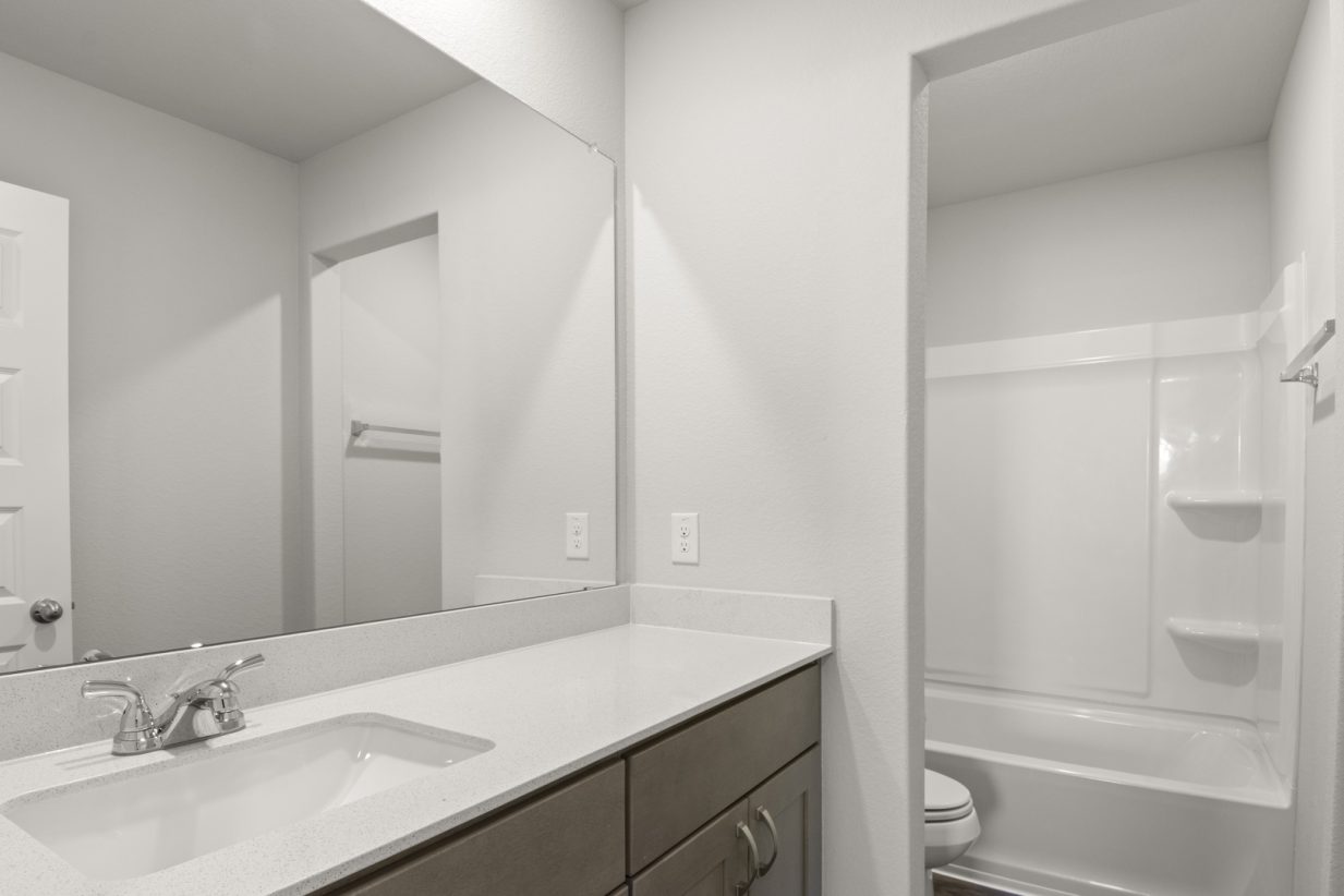 Image of a bathroom with a semi private water closet and white vinyl shower, and a white vanity with a mirror and brown cabinets
