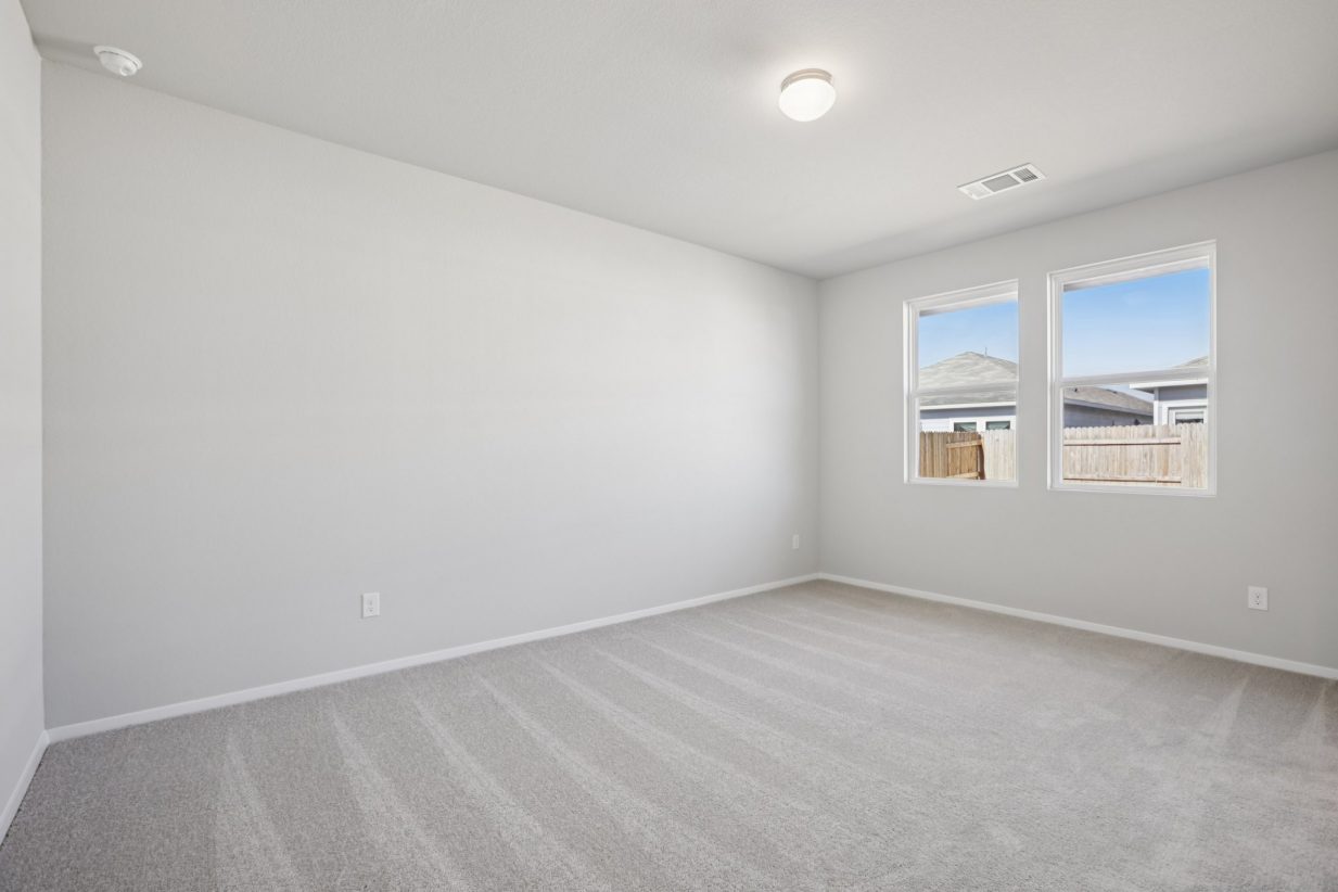 Image of a primary bedroom with light grey walls, tan carpeting, two windows and white trim