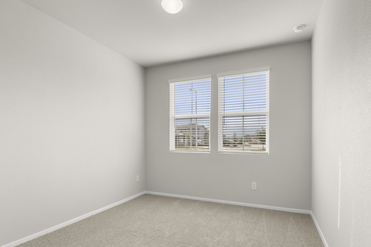 Image of a bedroom with tan carpeting, light grey walls and two windows