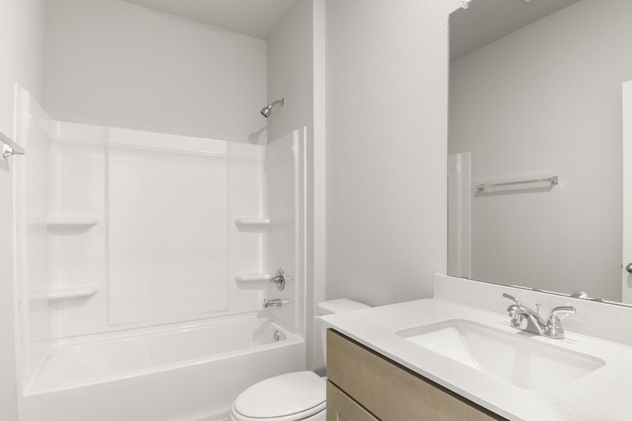 Image of a bathroom with a white shower and tub, a white vanity, light brown cabinets and a mirror