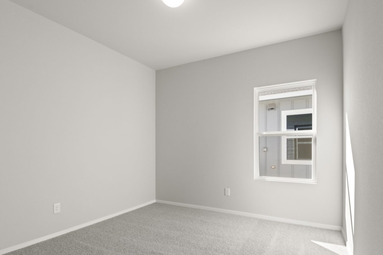 Image of a bedroom with light grey walls, tan carpeting, white trim and a window
